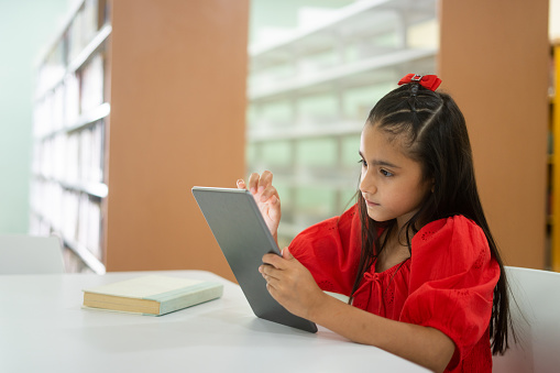 A cute little latin girl sitting and using a digital tablet.