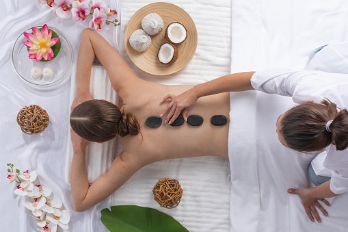 Top view of beautiful young woman lying on front with hot spa stones on her back. Beauty treatment concept.