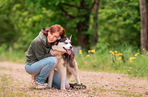 adult woman hugs her fluffy friend of the Siberian Husky on the road against the background of the forest.