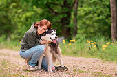 An adult woman hugs her fluffy friend of the Siberian Husky on the road against the background of the forest.