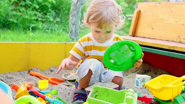 A little boy playing in the sandbox at the playground outdoors. Toddler playing with sand molds and making mudpies. Outdoor creative activities for kids