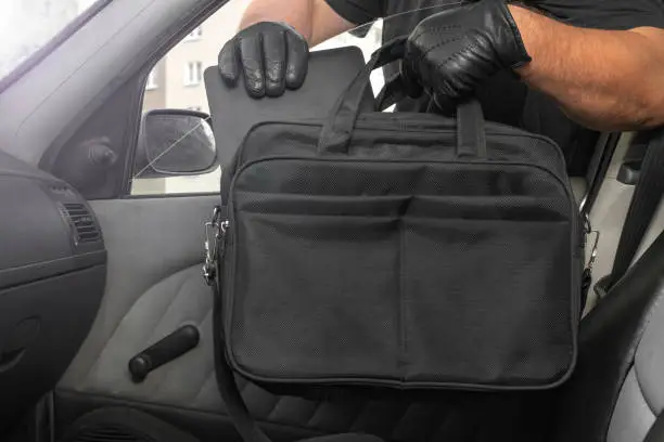 Thief steals a laptop bag from the passenger seat from an open car window. View from inside the automobile interior. Concept of robbery.