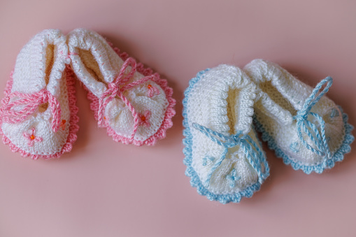 Istanbul, Turkey-August 5, 2022: Two pairs of hand-knitted white wool baby booties on a light pink background. Shot with Canon EOS R5.