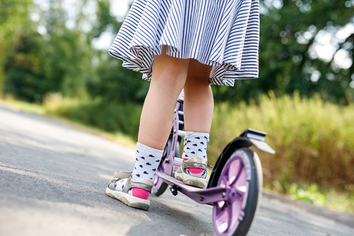 Closeup of active little preschool girl riding scooter on road in park outdoors on summer day. Seasonal child activity sport. Healthy childhood lifestyle.