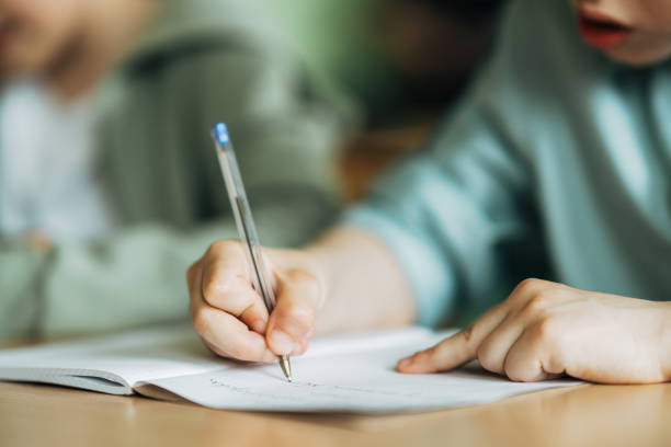 Close-up of a boy writing with a pen in workbook Close-up of a boy writing with a pen in workbook. Elementary schoolboy sitting on desk and studying in classroom. schoolboy stock pictures, royalty-free photos & images