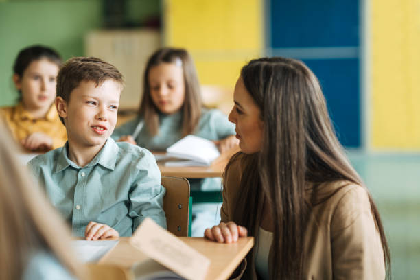 istock Elementary school teacher helping schoolboy at desk in lesson 1413476436