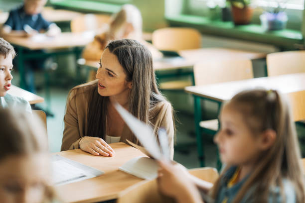 istock Elementary school teacher explaining to schoolboy at desk in lesson 1413476437