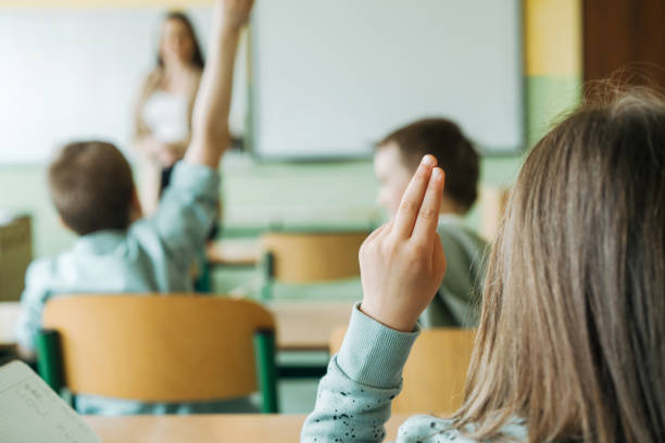 istock Elementary school children in classroom putting up hands for asking questions 1413476535