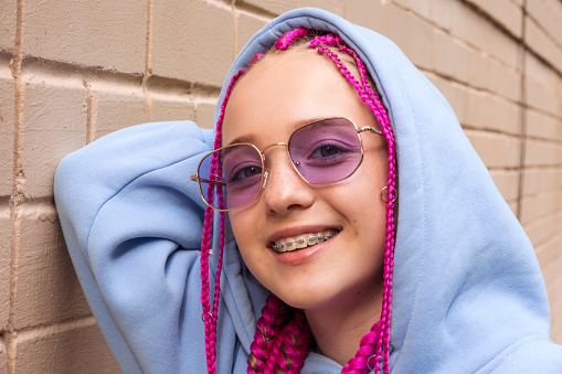 Portrait of a happy caucasian teenage hipster girl with pink braids and sunglasses against a pink brick wall.Summer concept.Generation Z style.
