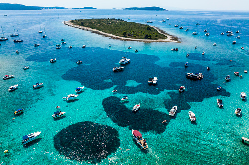 Incredible shades of blue and emerald colors with many anchored boats seen from a drone perspective in the Blue Lagoon during summer season in Croatia.