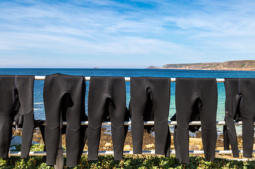 Wet suits hanging to dry on a railing, at Sennen beach in Cornwall