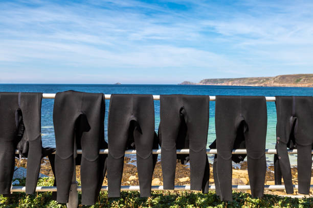 A row of wet suits drying at the beach, at Sennen in Cornwall Wet suits hanging to dry on a railing, at Sennen beach in Cornwall wetsuit stock pictures, royalty-free photos & images