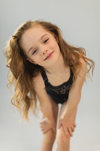 Little cute girl with long blonde curly hair in studio on white background. Beauty makeup with glitter. Childhood. Stylish child. Princess. Beautiful face. Lips gloss