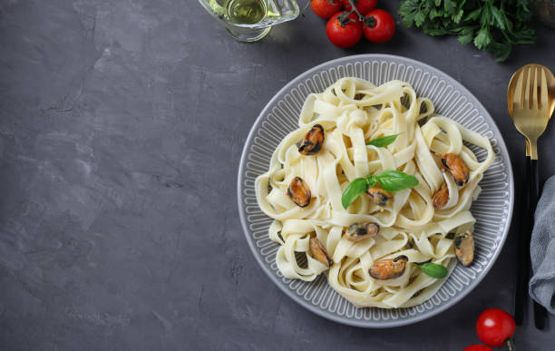 Tagliatelle pasta with mussels and basil on plate on gray background. Copy space stock photo