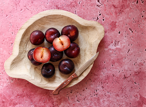 Istanbul, Turkey-August 3, 2022: Angelic plums on rustic wooden plate. The plate is on a dark pink rough concrete floor. Shot with Canon EOS R5.