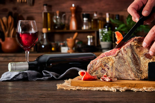 Man slicing Iberian pig ham leg on cutting board with bottle of red wine on rustic wooden table Man slicing Iberian pig ham leg on cutting board with bottle of red wine on rustic wooden table wine italian culture wine bottle bottle stock pictures, royalty-free photos & images