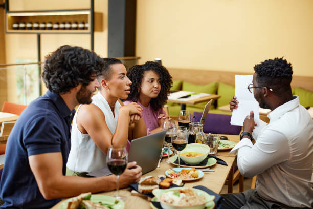 ein afrikanischer manager zeigt die jährlichen finanzen auf papier, während er während des mittagessens ein briefing mit mitarbeitern in einem restaurant hat. - restaurant chef gourmet dining stock-fotos und bilder