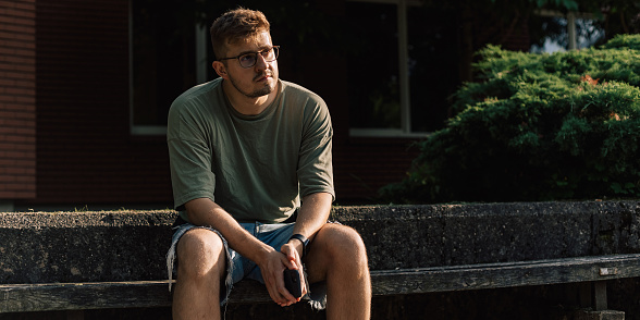 Male portrait of man wear t-shirt and eyeglasses using mobile phone outdoors. Lifestyle photography concept. Person is walking on the road in city