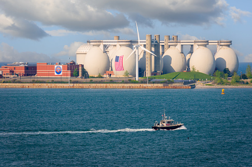 Boston, Massachusetts, USA- May 20, 2022- A small  pilot boat cruises past the twelve egg 12   egg-shaped anaerobic digesters, each 90 feet in diameter and approximately 130 feet tall,  of the MWRA water treatment plant on Deer Island in Boston Harbor.  This plant processes most of the waste water of the City and surrounding communities and has played a huge role in cleaning the harbor.