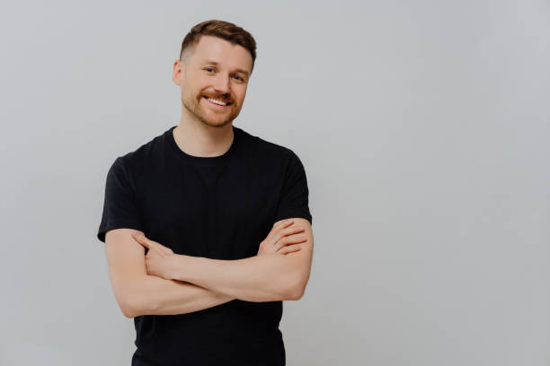 istock Horizontal shot of satisfied self assured man keeps arms folded smiles gladfully dressed casually enjoys day off poses against blue background with blank space. Handsome glad male model in studio 1413493884