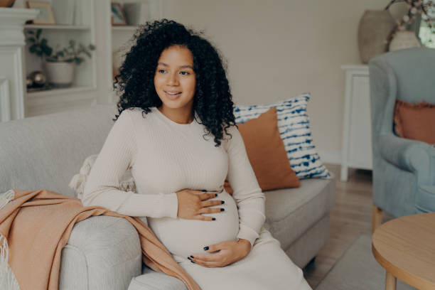 istock Smiling lovely african young future mom sitting on sofa 1413494658