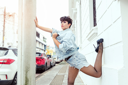 beautiful short-haired dancer woman in the city posing with a lot of flexibility in fashion outdoors in the city with blue jacket and heels modern, urban concept,