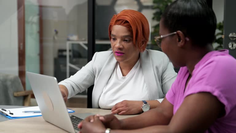 Over shoulder view female broker speaking to client using laptop