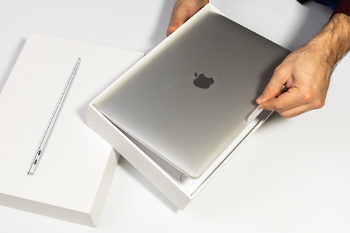 Saratov, Russia - February 26, 2022: take out new modern Macbook Air 13 inch with M1 processor from stylish packaging topview, white background. Advertising of modern technology and portable device.