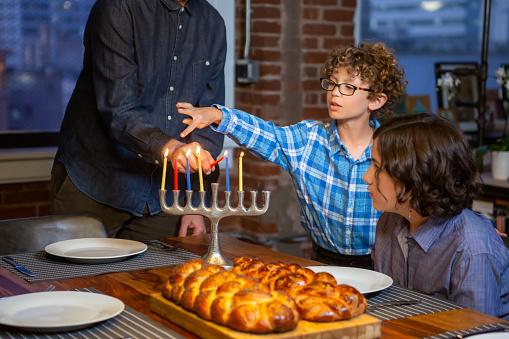 An adult re-lights a Hanukkah candle in a hanukiah to celebrate for the holiday while the children watch.