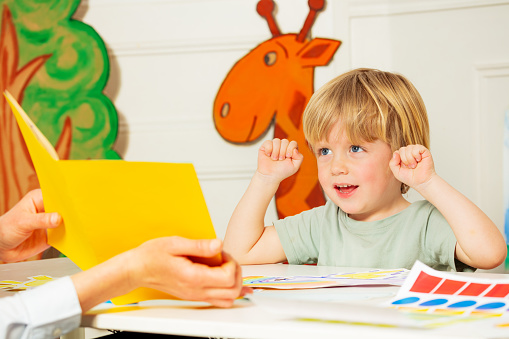 Early development lesson - little blond boy engaged in the process lift hands looking at the picture in the book