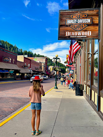 Deadwood, South Dakota, USA - July 7, 2022: A girl stands on the sidewalk of “Historic Main Street” eating ice cream on a hot summer afternoon.