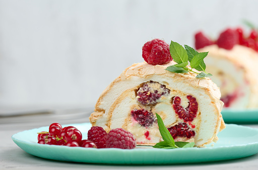 Baked meringue roll with red berries on a round plate, white background