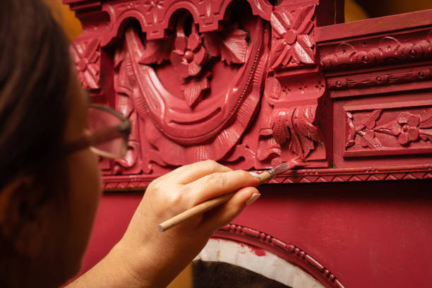 close-up de senhora de meia-idade pintando velho armário antigo ornamentado em vermelho com pincel fino pouco. oficina para reforma de móveis. nova vida para coisas antigas - patination - fotografias e filmes do acervo