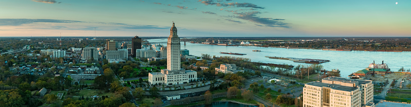Panoramic drone shot of Baton Rouge, Louisiana at sunrise, including the Mississippi River, the State Capitol Building and downtown office buildings.