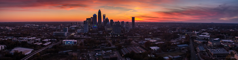 Panoramic drone shot of Charlotte, North Carolina at dusk, with the Uptown skyline silhouetted against a colorful sky. \n\nAuthorization was obtained from the FAA for this operation in restricted airspace.