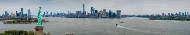 Aerial Panorama of New York Harbor Panoramic drone shot of New York Harbor on an overcast day, looking past the Statue of Liberty and Ellis Island towards Jersey City, Manhattan, and Brooklyn. new york city built structure building exterior aerial view stock pictures, royalty-free photos & images