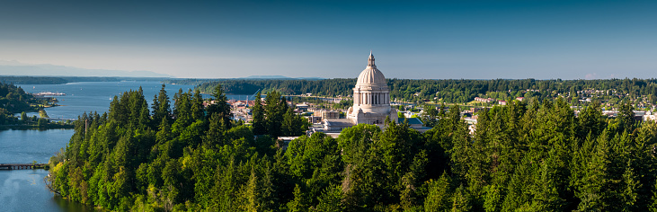 Panoramic drone shot of the state capitol building in Olympia, Washington on a summer afternoon, with the Puget Sound beyond.