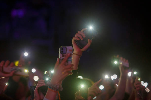 フラッシュをつけてスマートフォンを持ち、手を挙げている人 - popular music concert mobile phone smart phone telephone ストックフォトと画像