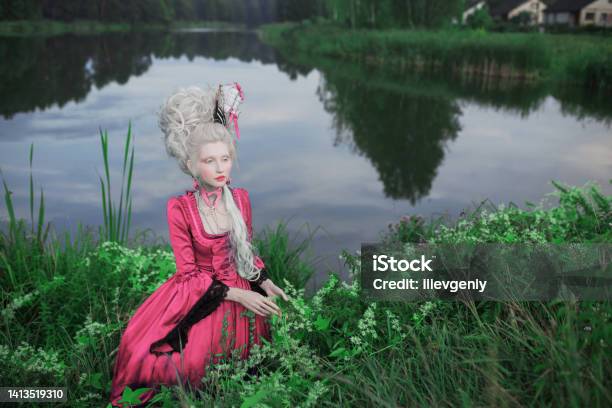 Renaissance Princess With Blonde Hair On Lake Background Beauty Makeup Fairytale Rococo Queen With Ship In Hairstyle On Nature Model In Pink Dress Woman With Historical Hair Style Sit In Grass Stock Photo - Download Image Now
