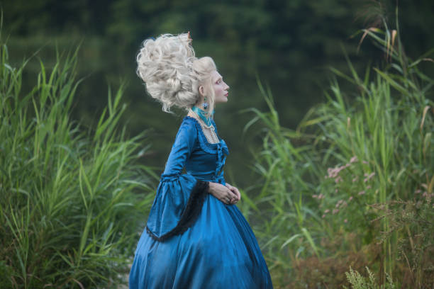 princesa renascentista com cabelo loiro no fundo do lago. maquiagem de beleza. rainha rococó de conto de fadas com navio em penteado sobre a natureza. modelo de vestido azul. mulher com estilo de cabelo histórico na ponte - princess hairstyle baroque style women - fotografias e filmes do acervo