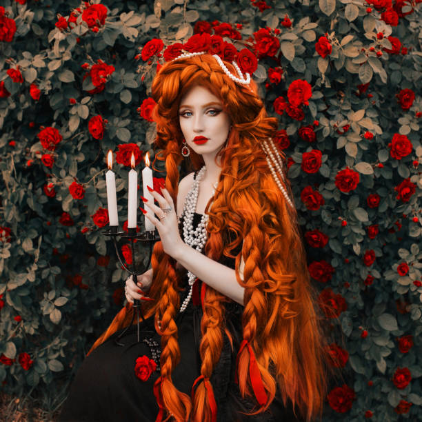 femme vampire rousse. longs cheveux bouclés. peau pâle. fille en robe noire sur fond fleur rose. beau modèle aux lèvres rouges. tenue renaissance pour halloween. coiffure. bijoux et bijouterie - renaissance women queen fashion photos et images de collection