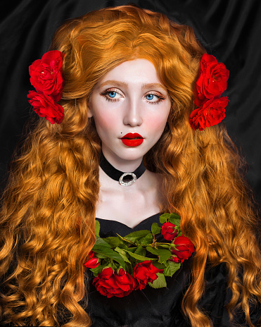Redhead fabulous woman. Long curly hair. Pale skin. Girl in choker and black dress on dark background. Beautiful model with red lips. Renaissance outfit. Hairstyle. Jewelry and bijouterie. Rose flower