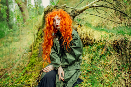 Redhead woman in raincoat on background of wet forest. Save earth. Green summer trees. Protection of nature. Tourist travel in rain coat. Save planet eco concept. Spring nature. Moss on tree