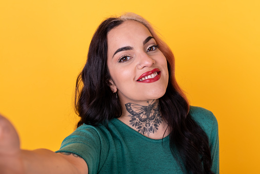 Portrait of an attractive woman making a selfie over yellow background. Studio shot.