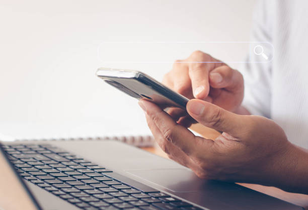istock Data Search Technology Search Engine Optimization. close up of a businessman working with a mobile phone and laptop computer to search for information on a wooden desk in a modern office. 1413525331
