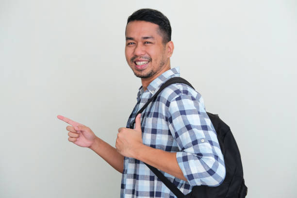 istock SIde view of asian man wearing backpack smiling while pointing forward 1413527097