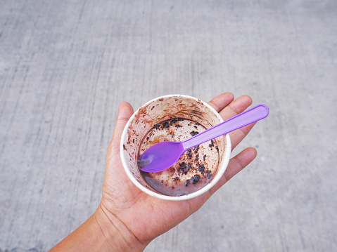 Paper cup of eaten chocolate ice cream with plastic spoon on hand holding. Street food.