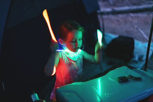 A girl has fun playing drums on her camp stove with glow sticks.