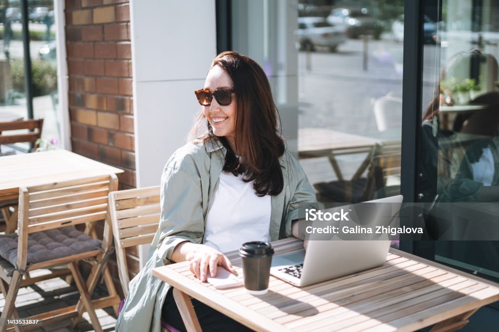 Adult smiling brunette business woman forty years in stylish shirt working on laptop in cafe at city street 40-44 Years Stock Photo