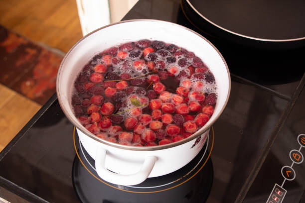 homemade fruit compote with cherry boils on the stove in the kitchen in a white saucepan, fruit compote stock photo